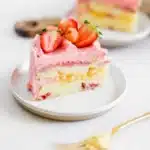 A slice of Strawberry Lemon Cake showing the moist lemon sour cream crumb with pink strawberry lemon cream cheese frosting and fresh strawberry garnish on a white plate