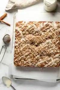 Apple Cider Coffee Cake Recipe stunning fall brunch coffee cake with gorgeous cream cheese swirl layer and golden brown sugar streusel topping cut to show the swirl cross-section in a white pan on marble