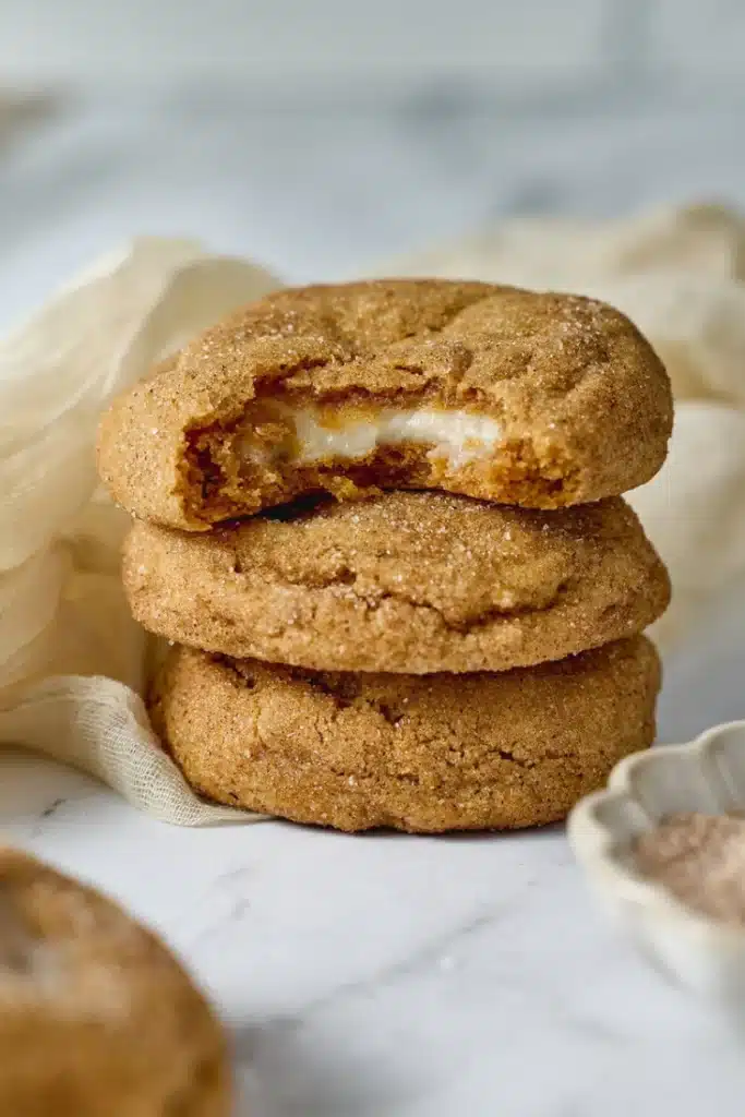 Pumpkin Cheesecake Cookie Recipe gorgeous open-faced fall cookies with beautiful golden maple cream cheese swirl on top and cinnamon sugar coating on a white plate on marble