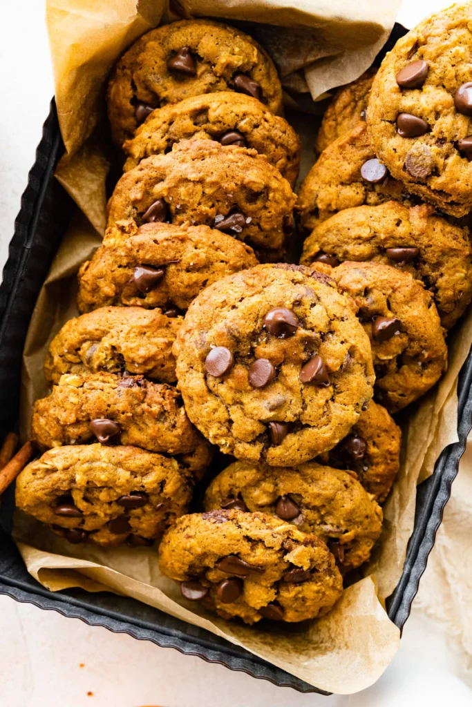 Home 7 Pumpkin Oatmeal Cookies hearty golden fall cookies with rolled oats and chocolate chips on a white plate on marble with small decorative pumpkins alongside