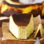 A slice of Burnt Basque Cheesecake showing the dramatically dark caramelized top and gloriously custardy creamy interior with no crust on a white plate
