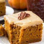 A slice of Pumpkin Cake with Caramel Cream Cheese Frosting showing the moist pumpkin spice crumb with silky caramel cream cheese frosting and caramel drip on a white plate